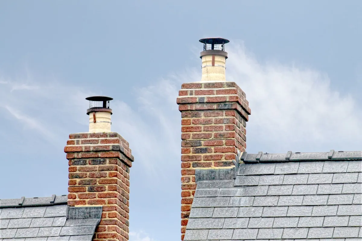 Close-up of traditional brick chimneys on a slate roof, highlighting potential moisture retention.